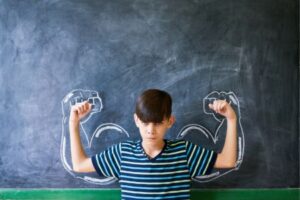 Kid with drawn muscles in front of chalk board.